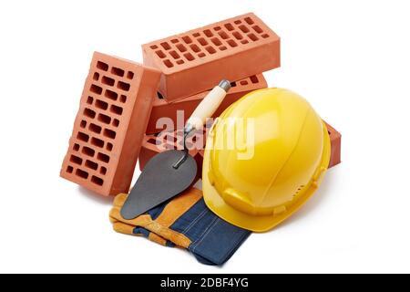Construction concept. Stack of new bricks with masonry trowel, construction yellow hard hat and protective  gloves on white background. Stock Photo