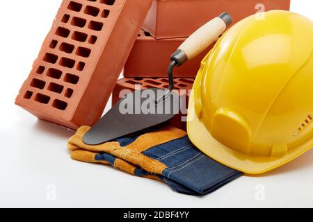 Construction concept. Stack of new bricks with masonry trowel, construction yellow hard hat and protective  gloves on white background. Stock Photo