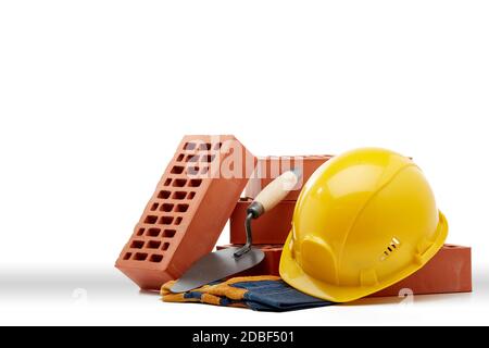 Construction concept. Stack of new bricks with masonry trowel, construction yellow hard hat and protective  gloves on white background with copy space Stock Photo