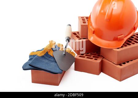 Construction concept. Stack of new bricks with masonry trowel, construction orange hard hat and protective  gloves on white background with copy space Stock Photo