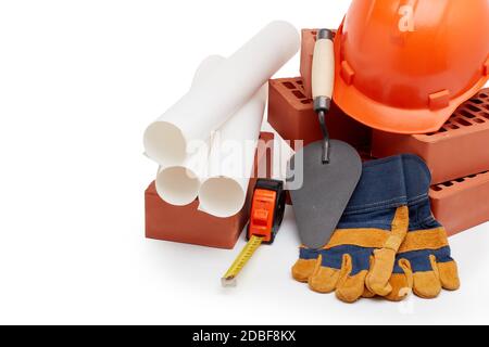 Construction concept. Stack of new bricks with masonry trowel, architectural blueprints, tape measure, construction orange hard hat and protective  gl Stock Photo