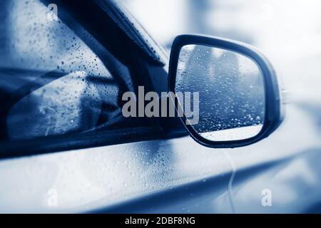 The light silver car drives fast in bad weather, and there are clear raindrops on the windows and on the rearview mirror. Melancholy. Stock Photo