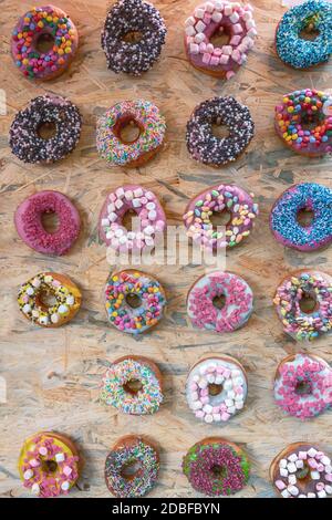 Twenty three donuts with different toppings in many colors and flavors on a wooden board Stock Photo
