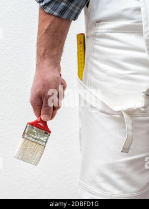 Caucasian house painter worker in white overalls, he holds the brush in his hand. Construction industry. Work safety. Stock Photo