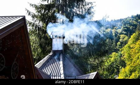 Dense Smoke Rises From the Chimney at the mountain view background. Village old house. Rural Scene. Suburban Village. Stock Photo