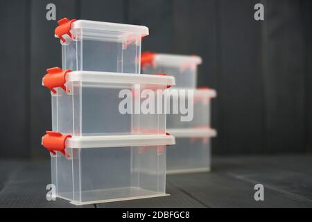 Clear plastic object storage boxes with orange accents stacked on floor and gray wooden background Stock Photo