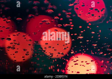 Raindrops on the windshield of the car with blurred colored lights in the background. Traffic and rainy weather on the road. Stock Photo
