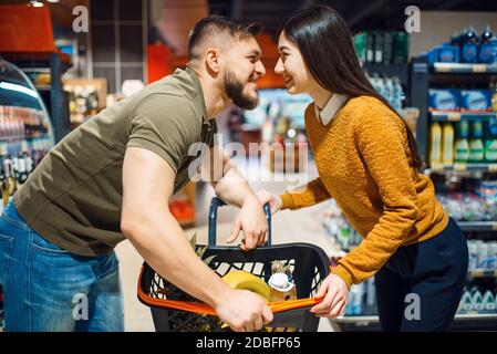 Love couple poses in grocery store. Man and woman with cart buying beverages and products in market, customers shopping food and drinks Stock Photo