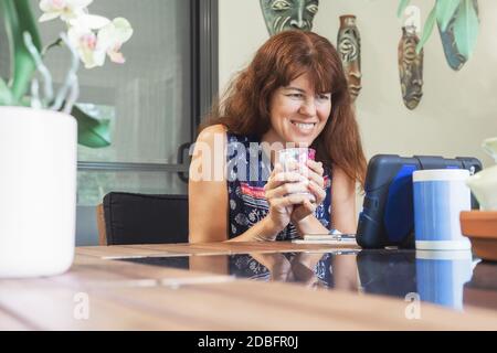 Happy woman having video chat on tablet sitting at the table with cup of tea or coffee. Stock Photo