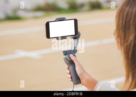 Woman hand holding gimbal with smartphone, blank screen. Taking pictures and live video. Vlog and video blogging concept Stock Photo