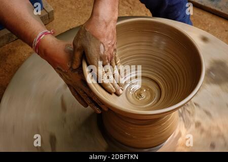 Pottery - skilled wet hands of potter shaping the clay on potter wheel. Pot, vase throwing. Manufacturing traditional handicraft Indian bowl, jar, pot Stock Photo