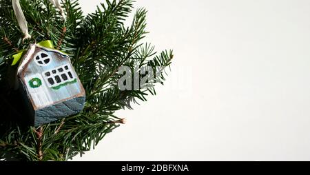 Wooden toy house on green branch of christmas tree. Christmas banner with decoration. Backround copy space for text. Stock Photo