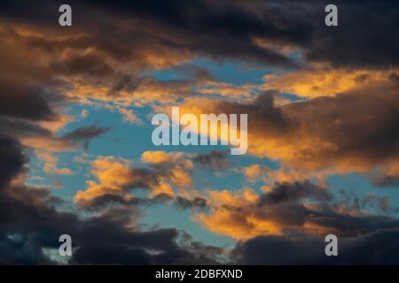 Dramatic colorful storm clouds illuminated rising of sun floating in blue sky. Natural weather, majestic cloudscape, meteorology background Stock Photo