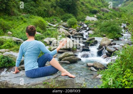 Yoga exercise outdoors -  woman doing Ardha matsyendrasanaasana asana - half spinal twist pose at tropical waterfall in Himalayas in India Stock Photo