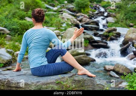 Yoga exercise outdoors - woman doing Ardha matsyendrasanaasana asana - half spinal twist pose at tropical waterfall in Himalayas in India Stock Photo