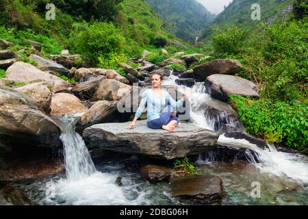 Yoga exercise outdoors - woman doing Ardha matsyendrasanaasana asana - half spinal twist pose at tropical waterfall in Himalayas in India Stock Photo