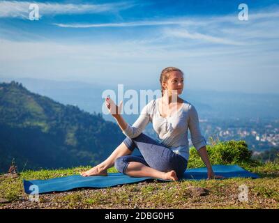 Yoga exercise outdoors -  woman doing Ardha matsyendrasanaasana asana - half spinal twist pose mountains in Himalayas in India in the morning Stock Photo