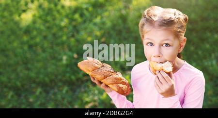 Little girl eating bread. Outdoors female portrait. Look at camera Stock Photo