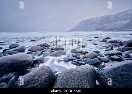 Waves of Norwegian sea surging on stone rocks at Unstad beach, Lofoten islands, Norway in winter storm. Long exposure Stock Photo