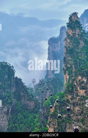 Famous tourist attraction of China - Zhangjiajie stone pillars cliff mountains in fog clouds with cable railway car lift at Wulingyuan, Hunan, China. Stock Photo