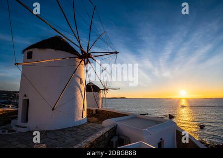 Scenic view of famous Mykonos town windmills. Traditional greek windmills on Mykonos island on sunset with dramatic sky, Cyclades, Greece. Walking wit Stock Photo