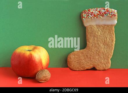 cookie in the shape of a santa stocking or for Saint Nicholas Day, green and red arrangement with apple, walnut and copy space Stock Photo