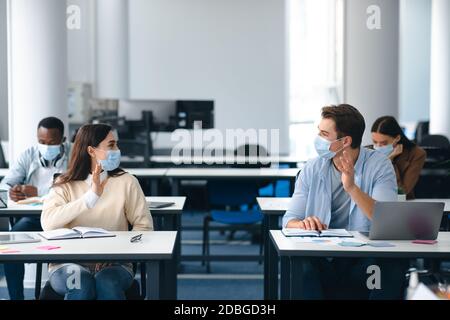 Diverse students wearing face masks greeting and waving Stock Photo