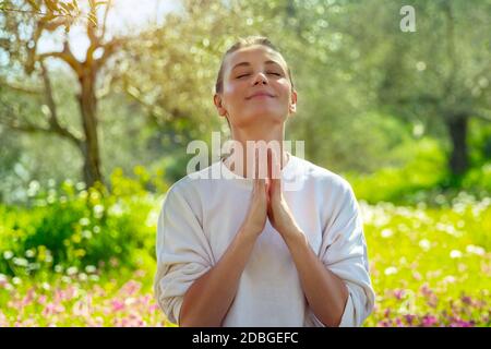 Portrait of a joyful woman with closed eyes meditating in a fresh blooming garden. Unity of a mind, body, and spirit. Calmness and peacefulness concep Stock Photo