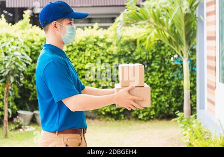 Asian delivery express courier young man use giving boxes to woman customer he wearing protective face mask at front home, under curfew quarantine pan Stock Photo