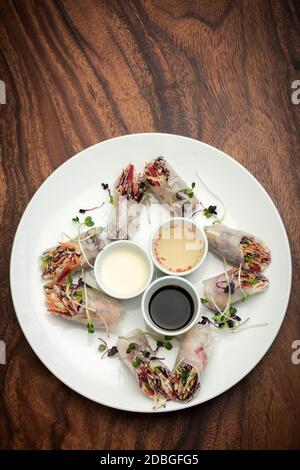 asian fresh vegetable vegan spring rolls with sauces on wood restaurant table background in vietnam Stock Photo