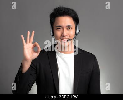 Smiling young asian businessman talking on headset and showing ok sign Stock Photo