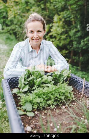 beautiful woman posing next to raised garden bed and her fresh vegetables Stock Photo