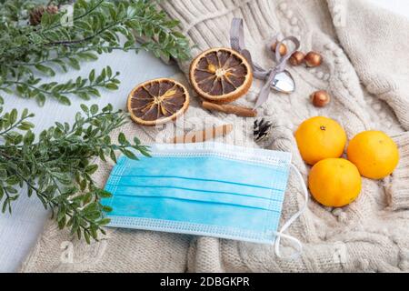 Medical mask and accessories for the New Year, a green twig, dry oranges, tangerines, a woolen sweater. Flatley on a white background. High quality photo Stock Photo