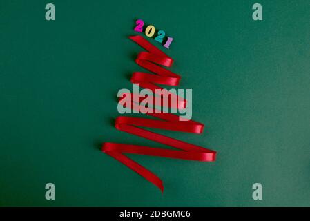 Christmas tree made from silk red ribbon on a bright green backdrop. Merry Christmas and Happy New Year festive background with empty space for text. Stock Photo