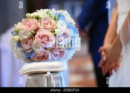 Bridal posy on a cushion with groom and bride in the background holding hands with selective focus to the flowers Stock Photo