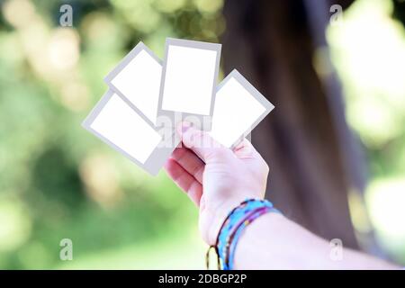 Hand holding up four blank instant photo frames fanned out against outdoor greenery with selective focus in close up Stock Photo