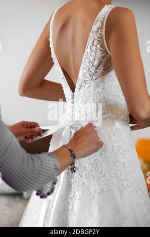 Maid of Honour helping the bride to dress in her elegant white wedding gown tying the bow at the back in a close up on her hands Stock Photo