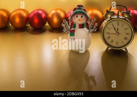 Christmas decoration with alarm clock orange, glass snow man, orange and and red baubles on golden background for text Stock Photo
