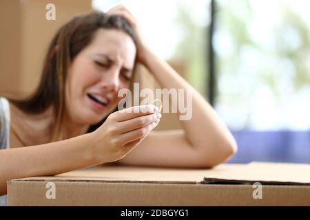 Sad wife complaining moving home after divorce holding wedding ring surrounded by boxes Stock Photo