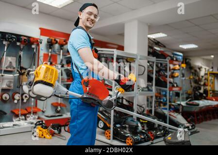 Male worker holds gas trimmer in tool store. Choice of professional equipment in hardware shop, electrical instrument supermarket Stock Photo