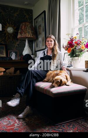 Interior designer Flora Soames and her dog Humbug, photographed at her Wiltshire home. Flora wears Carrier Company dungarees, With Nothing Underneath Stock Photo