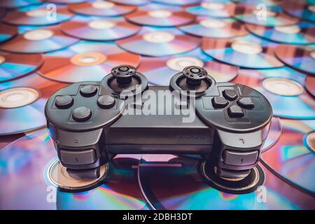 An old, worn out joystick from a game console lies on discs with video games Stock Photo