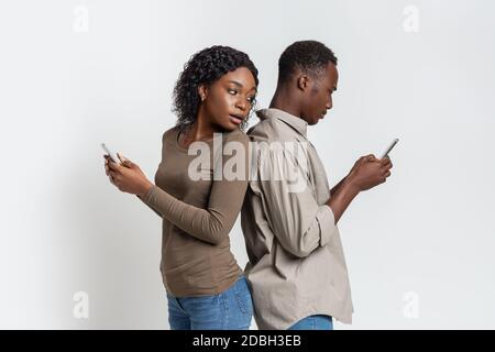 Black couple standing back to back, using smartphones Stock Photo