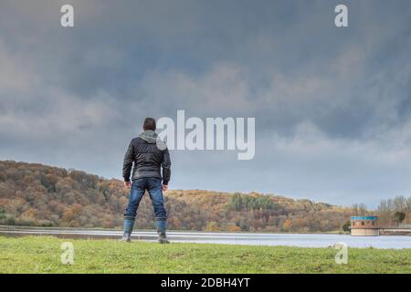 rear view of a menacing man looking over water with moody clouds above Stock Photo