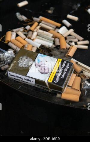 cigarettes - Cigarette butts and empty packet with health warnings - in rainwater on top of whisky barrel outside pub - Scotland, UK Stock Photo