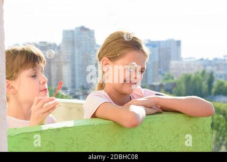 Girl blowing soap bubbles one of which burst at the face of another girl Stock Photo