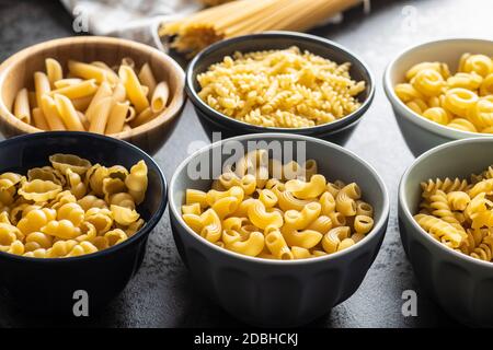 Various types of raw italian pasta in bowls on kitchen table. Stock Photo