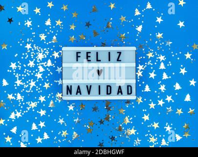 Light box with Feliz Navidad phrase, Spanish Merry Christmas on blue background with confetti. Stock Photo