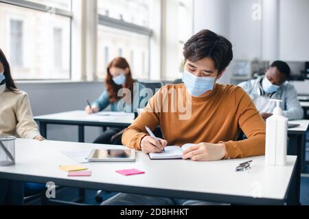 Asian male student in mask sitting at desk in classroom Stock Photo