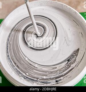 Home painter is mixing various colors in the basket with help of drill during renovation to paint wall. Handyman mixes paints with mixer. Stock Photo